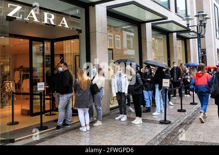 Münster, NRW, Germany. 22nd May, 2021. Long queues have formed outside a 'Zara' store. Crowds gather in the historic city centre of Münster, despite heavy rain, as it becomes the first city in North Rhine-Westphalia to be allowed to open up indoor drinking and dining (with negative test or vaccination), and shopping without a test or appointment (but numbers are restricted). Münster currently has one of the lowest covid incidence rates in NRW at 17/100k and has become a 'model region' to trial slow re-opening of hospitality venues. Credit: Imageplotter/Alamy Live News Stock Photo