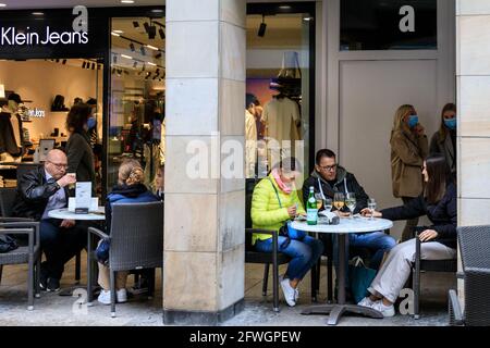 Münster, NRW, Germany. 22nd May, 2021. People in an outdoor cafe. Crowds gather in the historic city centre of Münster, despite heavy rain, as it becomes the first city in North Rhine-Westphalia to be allowed to open up indoor drinking and dining (with negative test or vaccination), and shopping without a test or appointment (but numbers are restricted). Münster currently has one of the lowest covid incidence rates in NRW at 17/100k and has become a 'model region' to trial slow re-opening of hospitality venues. Credit: Imageplotter/Alamy Live News Stock Photo