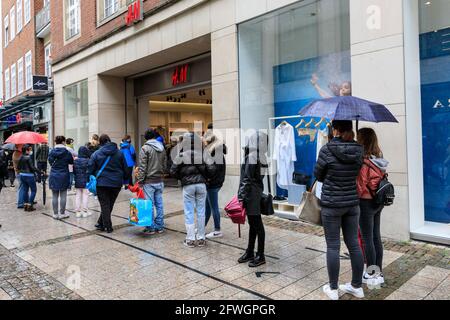 Münster, NRW, Germany. 22nd May, 2021. Long queues have formed outside a 'H&M' store. Crowds gather in the historic city centre of Münster, despite heavy rain, as it becomes the first city in North Rhine-Westphalia to be allowed to open up indoor drinking and dining (with negative test or vaccination), and shopping without a test or appointment (but numbers are restricted). Münster currently has one of the lowest covid incidence rates in NRW at 17/100k and has become a 'model region' to trial slow re-opening of hospitality venues. Credit: Imageplotter/Alamy Live News Stock Photo