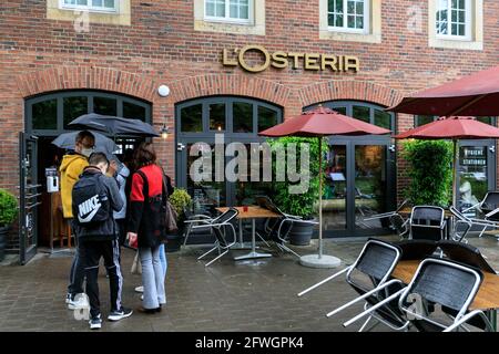 Münster, NRW, Germany. 22nd May, 2021. A queue outside popular restaurant L'Osteria. Crowds gather in the historic city centre of Münster, despite heavy rain, as it becomes the first city in North Rhine-Westphalia to be allowed to open up indoor drinking and dining (with negative test or vaccination), and shopping without a test or appointment (but numbers are restricted). Münster currently has one of the lowest covid incidence rates in NRW at 17/100k and has become a 'model region' to trial slow re-opening of hospitality venues. Credit: Imageplotter/Alamy Live News Stock Photo