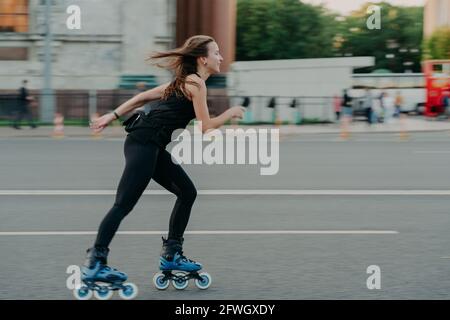 Full length shot of young slim woman rollerblades along asphalt on street enjoys speed spends free time on favorite hobby poses outdoors breathes Stock Photo
