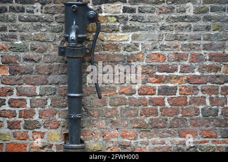 Old fashioned cast iron water pump with handle against the ancient brick wall of Belfort van Brugge the medieval bell tower of Bruges in Belgium. Stock Photo