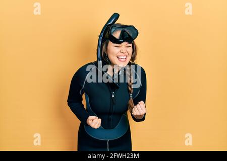 Young hispanic girl wearing diver neoprene uniform celebrating surprised and amazed for success with arms raised and eyes closed Stock Photo