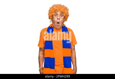 Senior hispanic man football hooligan cheering game scared and amazed with open mouth for surprise, disbelief face Stock Photo