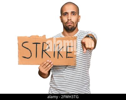 Hispanic adult man holding strike banner cardboard pointing with finger to the camera and to you, confident gesture looking serious Stock Photo