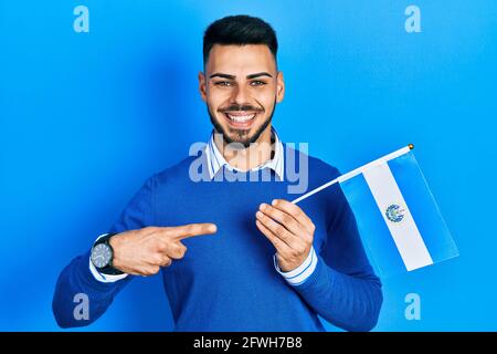 Young hispanic man with beard holding el salvador flag smiling happy pointing with hand and finger Stock Photo