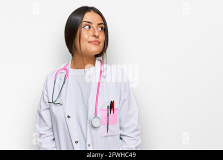 Beautiful hispanic woman wearing doctor uniform and stethoscope smiling looking to the side and staring away thinking. Stock Photo