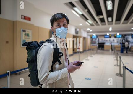 Flight rules during Covid-19 pandemic only in protective face mask. New normal concept. Masked man with phone in hand and backpack stand in line to Stock Photo