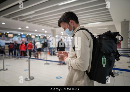 Flight rules during Covid-19 pandemic only in protective face mask. New normal concept. Masked man with phone in hand and backpack stand in line to Stock Photo