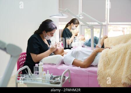 Professionals working with a clients in beaty salon. Woman lying on cosmetologiacal coach during lashes enlarging Stock Photo