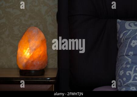 Himalayan pink salt lamp on the bedside table in the bedroom. Stock Photo
