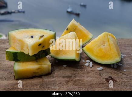 Fresh juicy yellow watermelon cut into triangles on old wooden table at balcony with city view. Tropical fruits, Select focus. Stock Photo