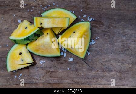 Fresh juicy yellow watermelon cut into triangles on old wooden background. Tropical fruits, Top view, Select focus. Stock Photo
