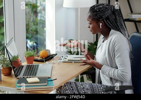 Pretty young female university student with long braids having online meeting with fellow students on big project Stock Photo