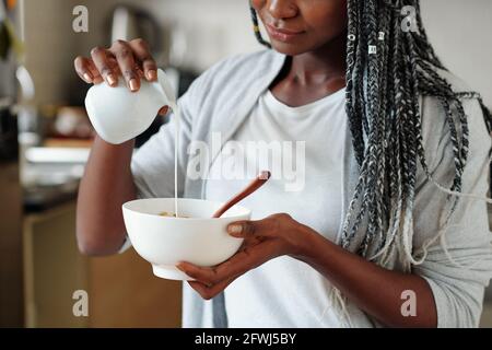 Cropped image of young woman pouring fresh milk in bowl with cornflakes or granola Stock Photo