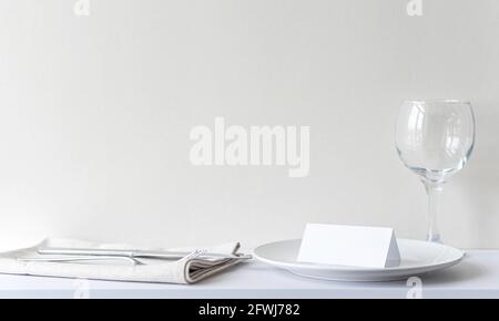 Blank invitation card on white plate in restaurant. Interior of restaurant with table, cutlery before celebrate, mockup, space for text Stock Photo
