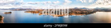 Sunset over Jindabyne town on Jindabyne lake of Snowy river in Australia - wide aerial panorama. Stock Photo