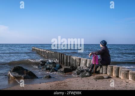 Old lady with a cane sitting on the seashore and gazing at the horizon. Stock Photo