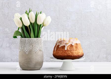 Bouquet of white tulips in grey ceramic vase and traditional Easter cake on the table. Festive decor Stock Photo