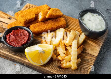 Fish fingers and Chips british fast food with tartar sauce set, on wooden cutting board, on gray background Stock Photo