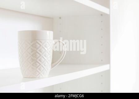 A white ceramic mug standing on an empty shelf. Home cleaning Stock Photo