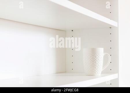 A white ceramic mug standing on an empty shelf. Home cleaning Stock Photo