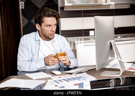 Concentrated male freelancer doing paperwork, sitting at the desk in home office. Focused young businessman or student working or studying distantly Stock Photo