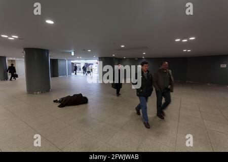 Marunouchi, Japan. 30th Jan, 2015. Salarymen or office workers walk past a Japanese homeless man sleeping on the floor in the shopping arcades under Tokyo Station. (Photo by Damon Coulter/SOPA Images/Sipa USA) Credit: Sipa USA/Alamy Live News Stock Photo