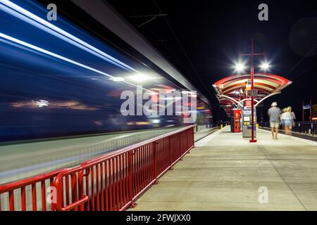 A light-rail train leaving the station with some passengers walking by Stock Photo