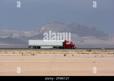 Bold red and white truck travels on highway through haze of blowing dust Stock Photo