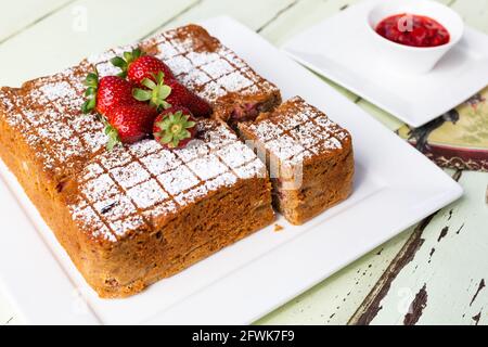 Square cake with cut slice on white plate with strawberries on top and couli on the side Stock Photo