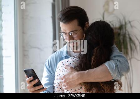 Dishonest young man using phone while cuddling wife. Stock Photo
