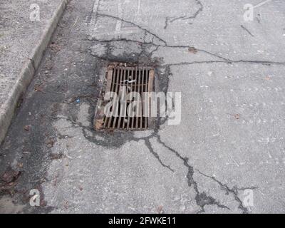 Rusty storm drain grate in cracked asphalt Stock Photo