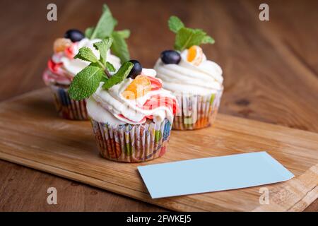 three cupcakes with a business card template on a wooden stand. Stock Photo