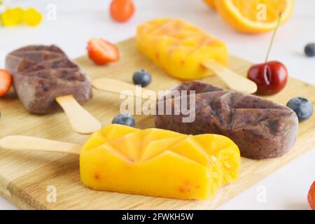 Group of homemade raspberry, cherries,strawberries, oranges, vanilla popsicles on a paddle board, frozen fruit juice, selective focus, white marble ba Stock Photo