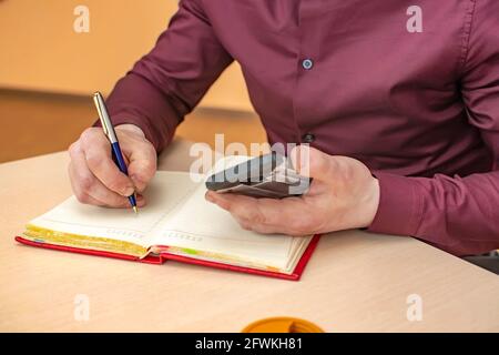 view of the hand of a business person with a writing pen in an office room, who writes notes in a notebook Stock Photo