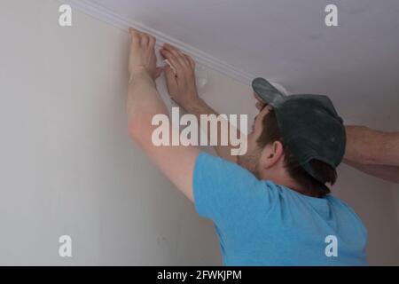 Man putting white ceiling skirting on ceiling Stock Photo