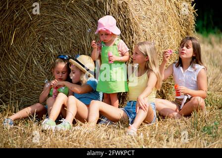 Lifestyle. Children. Five girls outdoors by rolled hay bale on the farm. Stock Photo