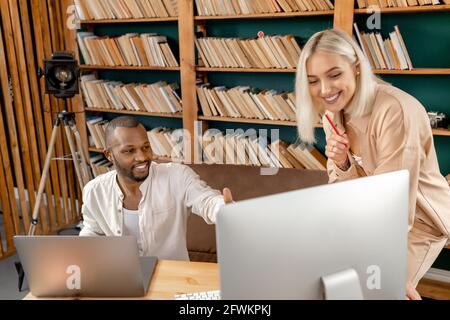 Happy multiethnic colleagues discussing a project, talking about ideas, smiling, making notes. Successful coworkers using laptop, doing some paperwork Stock Photo