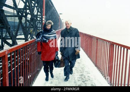 Two people crossing the river Thames, London, on the footbridge alongside the Hungerford railway bridge (since replaced), in falling snow Stock Photo
