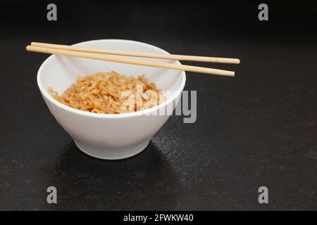 A kitchen bowl with ready-to-eat Chinese noodles. On the bowl are some oriental chopsticks. It is placed on a black granite bench in a kitchen and is Stock Photo