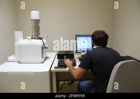Young man scientist working with scanning electron microscope. Laboratory technician observing samples with a SEM. Stock Photo