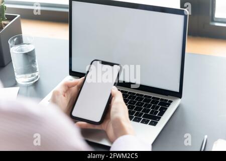 Close up businesswoman using smartphone and laptop with screen mockup Stock Photo