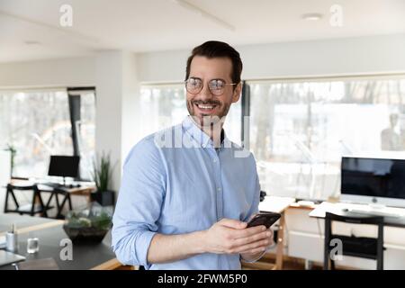 Excited dreamy businessman in glasses distracted from phone in office Stock Photo