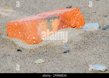 An orange red brick resting on a sandy beach. Sunny day. Stock Photo