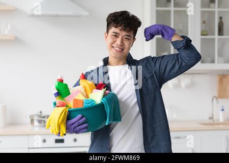 Positive asian guy with cleaning supplies showing muscles Stock Photo