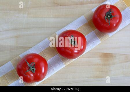 Three fresh ripe red tomatoes on linen cloth top view close up on wooden table Stock Photo