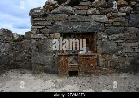 Old rusted cooking range and blue pot in ruins of stone cottage. Wall and roof are missing, showing blue sky. Exposed to elements. Isle of Lewis. Stock Photo