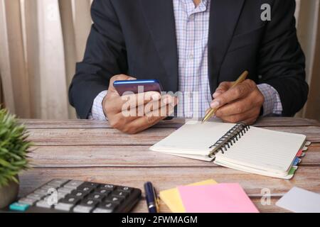 young man using smart phone and writing on notepad while sited  Stock Photo