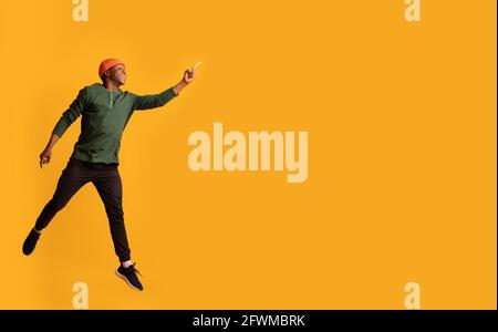 Look There. Excited African Guy Jumping And Pointing Aside At Copy Space Stock Photo